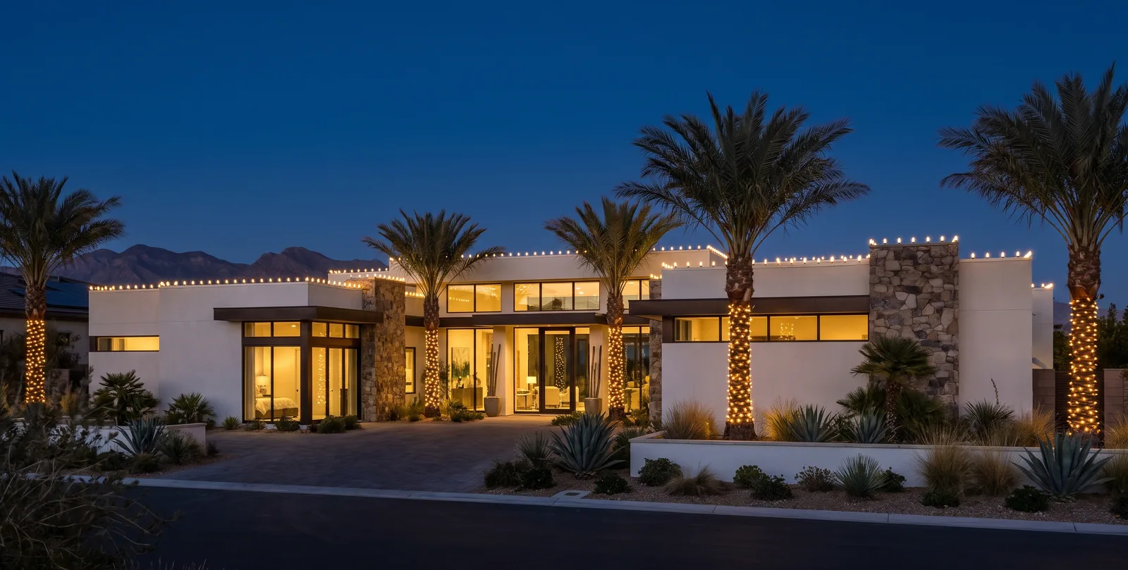 Single-story modern home with C9 bulbs along every parapet and five palms wrapped in warm white mini lights