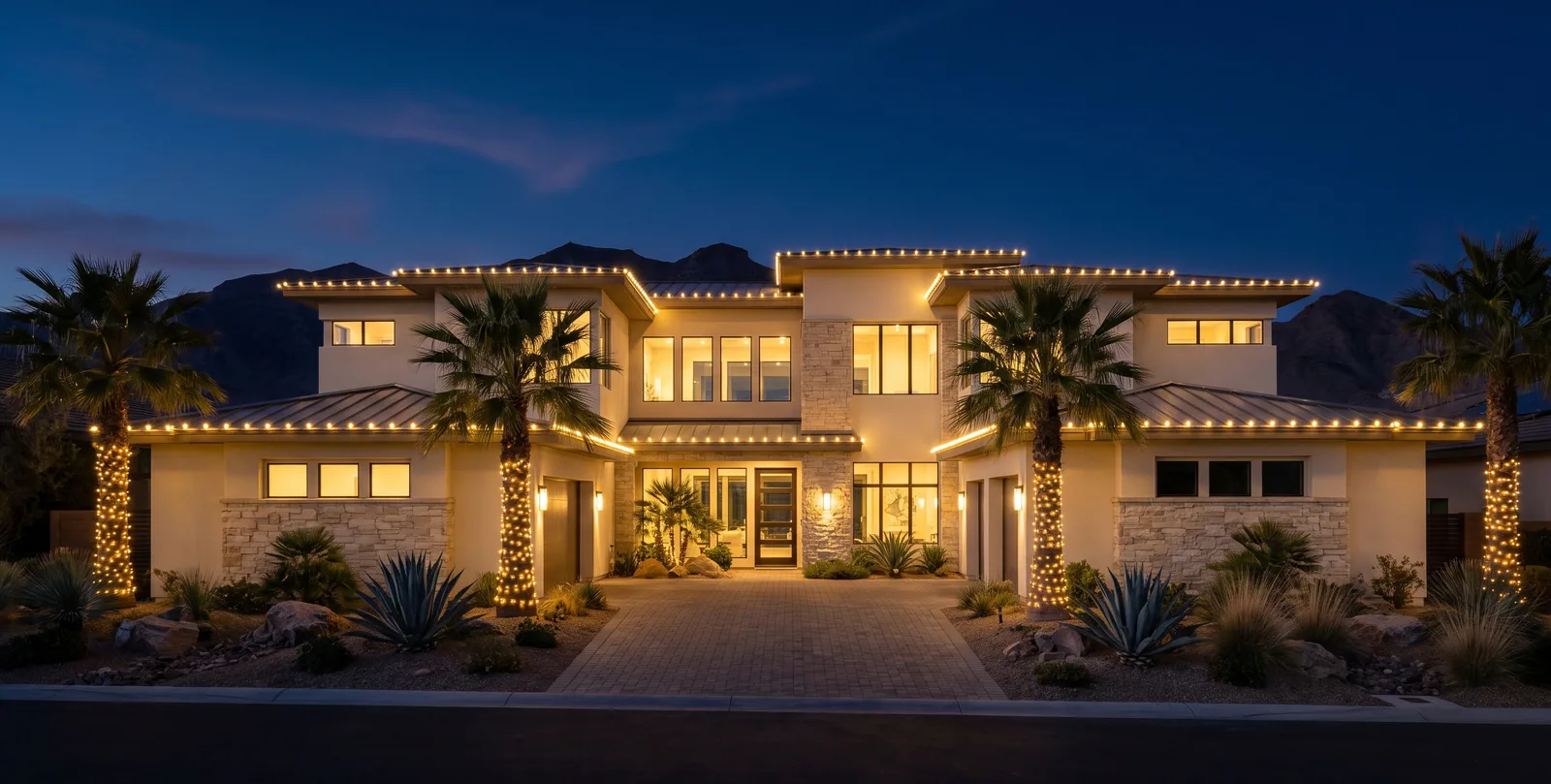 Two-story desert-modern home at blue hour with warm white C9 Christmas lights along every roofline and palm trunks wrapped in mini lights